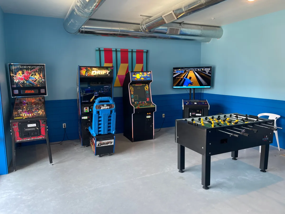 A playful entertainment area featuring arcade machines, a foosball table, and vibrant wall decorations. The lively space is designed for socializing, games, and friendly competition, making it a fun zone for teens and kids while adults unwind elsewhere.