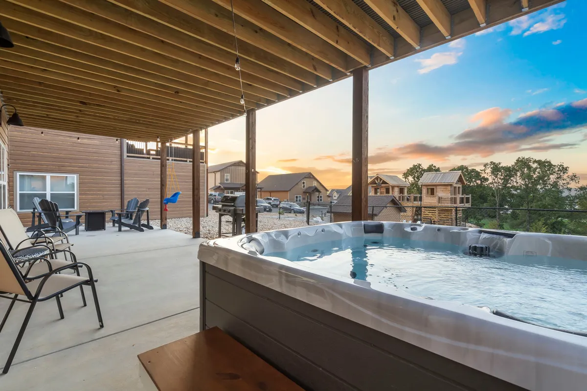 An inviting exterior patio showcases a private hot tub and comfortable outdoor seating, all set against a backdrop of rolling hills and a glowing sunset. The area is surrounded by nature, creating an atmosphere of tranquility and luxury.