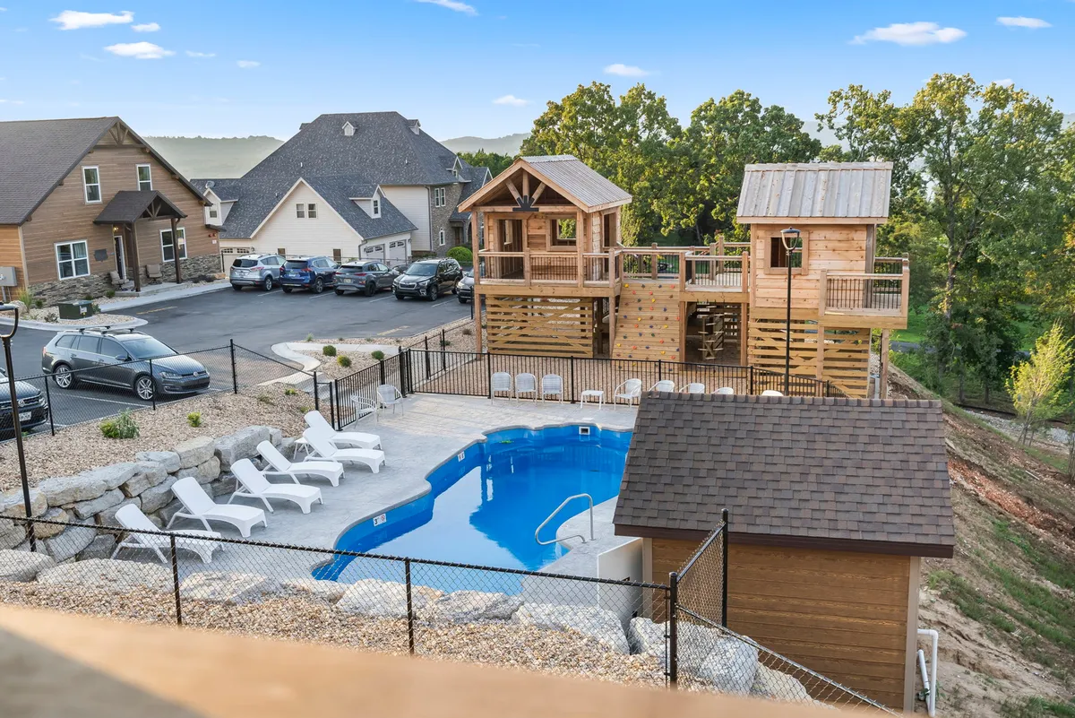 A lively exterior scene showcasing a sparkling outdoor swimming pool surrounded by lounge chairs, with a charming playhouse structure nearby. Children are seen playing and swimming while adults relax by the pool, creating a joyful atmosphere as the sun sets.