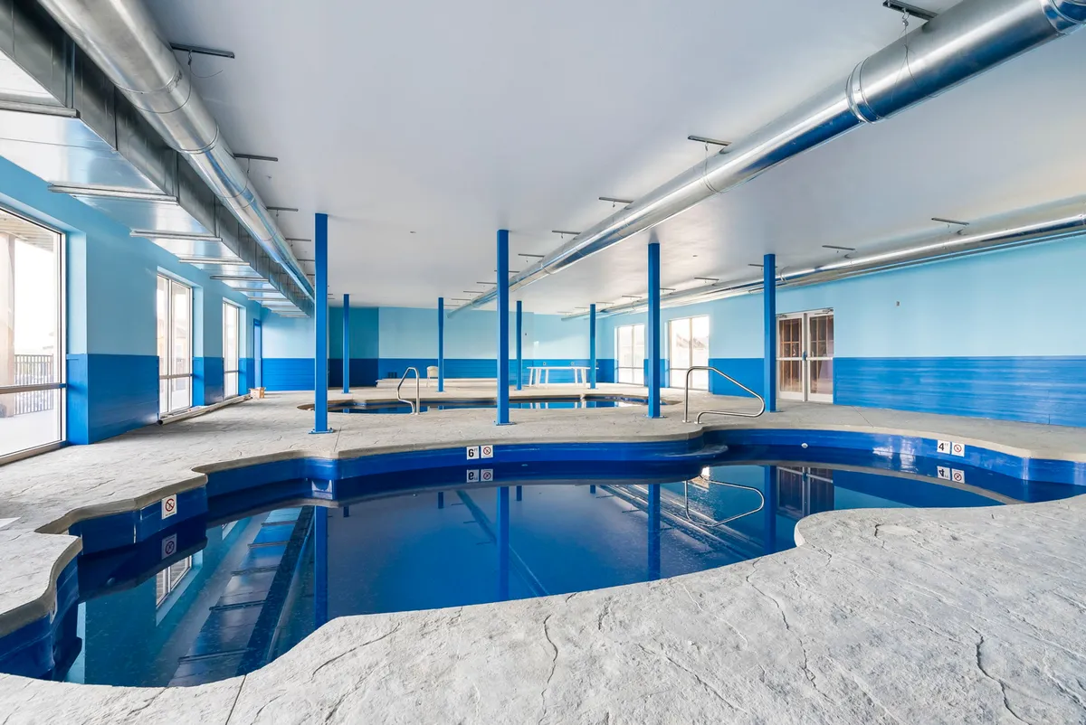 An inviting indoor swimming pool space with blue walls and large windows letting in natural light. The pool is ready for swimming, with ample room for both energetic play and peaceful relaxation, regardless of the season.