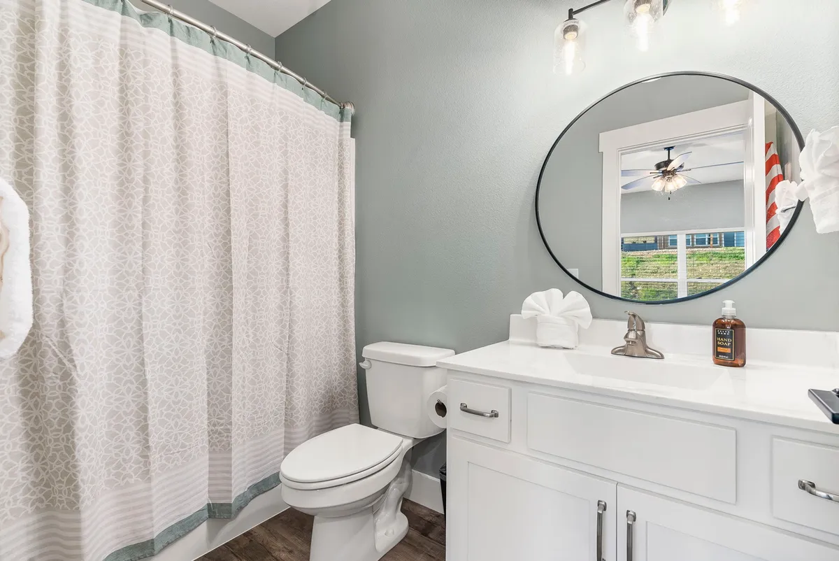 A modern bathroom highlighted by a round mirror, sleek white vanity with under-sink storage, stylish light fixtures, and a shower curtain. The space is bright, clean, and inviting—emphasizing quality fixtures and self-care.