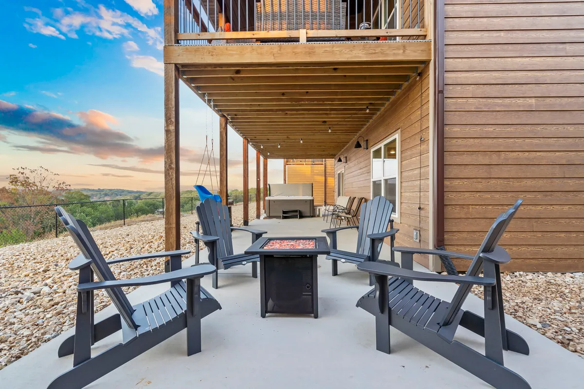 A cozy exterior fire pit area set on a wooden deck, surrounded by Adirondack chairs and overlooking a tranquil landscape. The scene invites guests to gather, relax, and enjoy starlit evenings in a communal atmosphere.