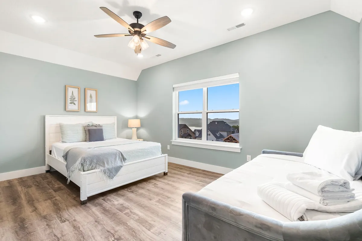 A spacious bedroom with a large bed in light gray bedding, a daybed neatly arranged with towels, and a generous window with a view, creating a bright and inviting atmosphere. The room feels flexible, perfect for families or groups.