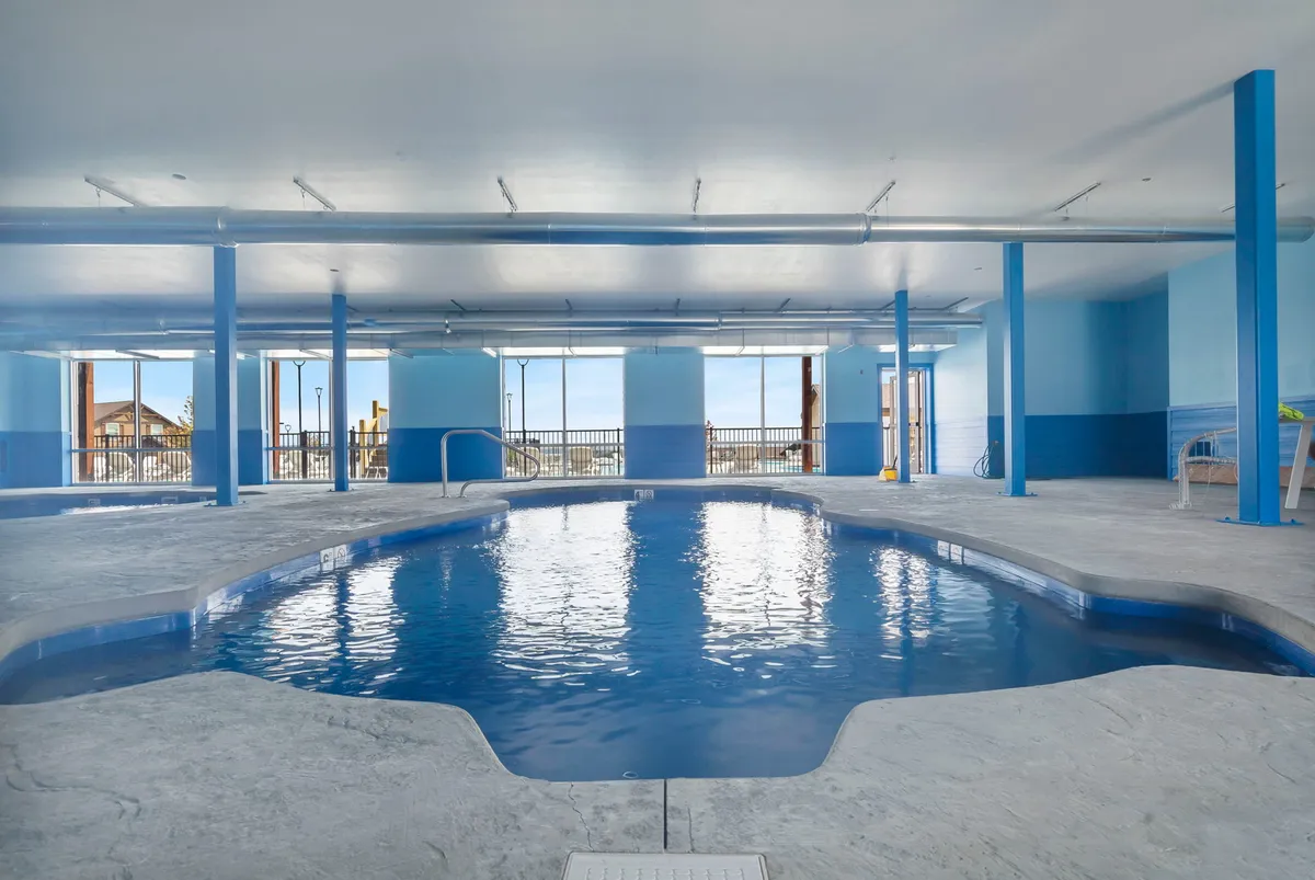 This interior photo features a bright, inviting indoor swimming pool with large windows letting in natural light. The tranquil setting includes smooth concrete surfaces and poolside seating, ideal for year-round relaxation, regardless of the weather outside.