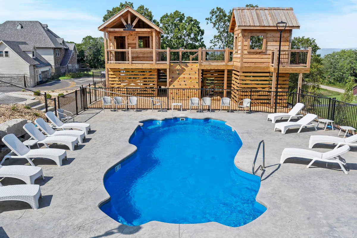 This image shows a vibrant outdoor resort pool surrounded by wooden playhouses and lounge chairs. Children can be seen playing, while families gather nearby, creating a lively, fun-filled atmosphere. The scene captures the essence of summer recreation with a focus on both swimming and play.